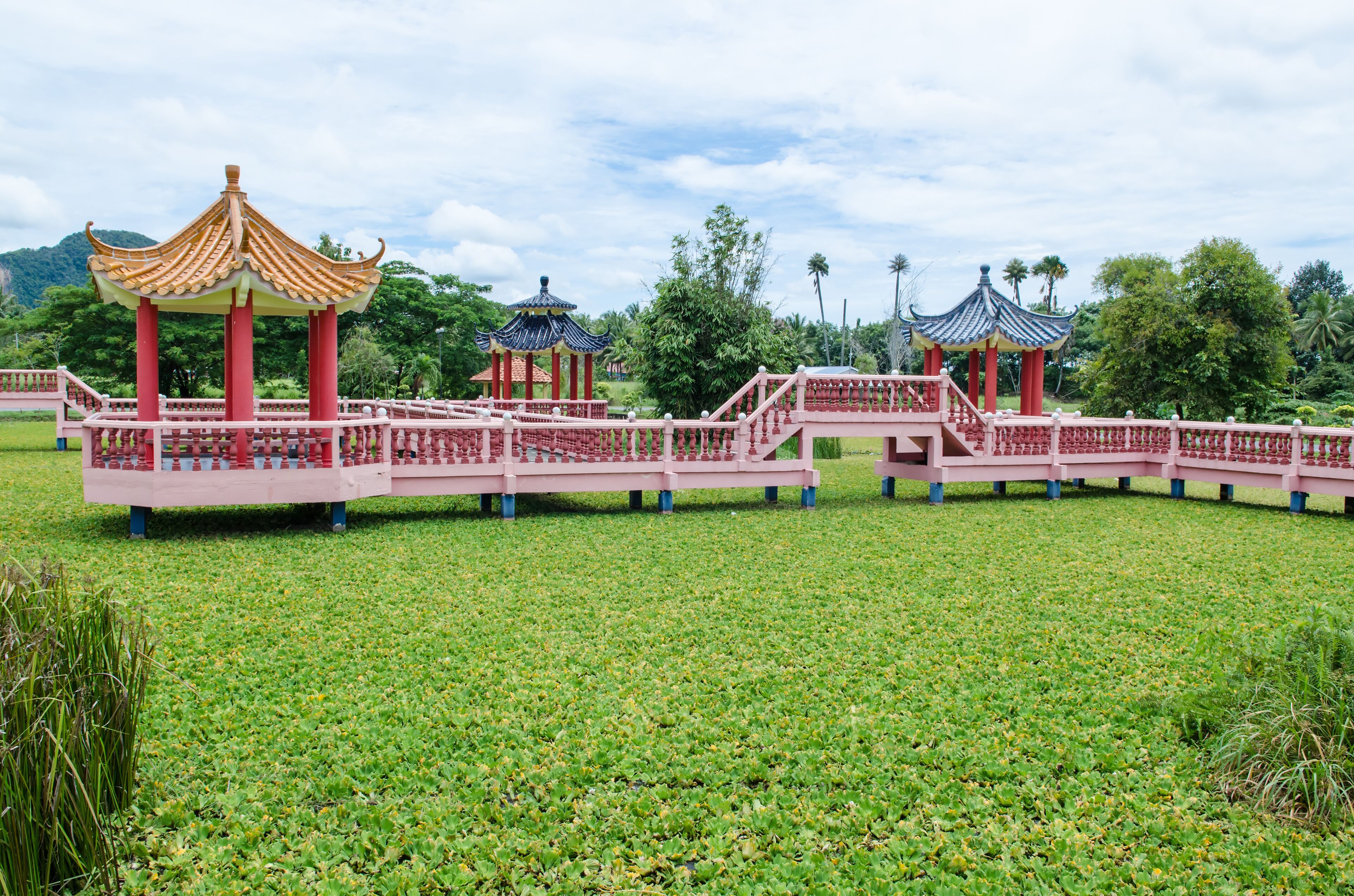 A traditional Chinese pavilion with a red roof and golden accents, surrounded by lush greenery and a clear sky.