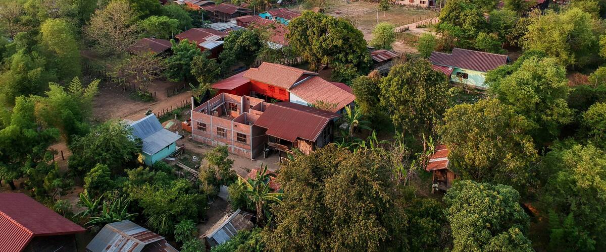 A rural village with scattered houses, dense greenery, and distant hills.
