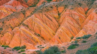 Un paysage composé de formations rocheuses aux couches distinctes, aux teintes orange et rouge éclatantes, et entouré d’une végétation verte clairsemée.