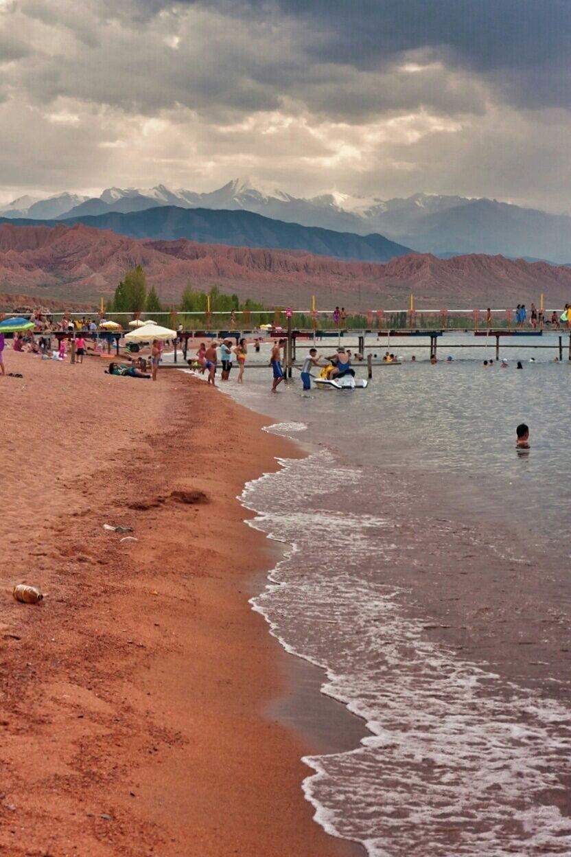 A beach with people, a body of water, and mountains in the background.