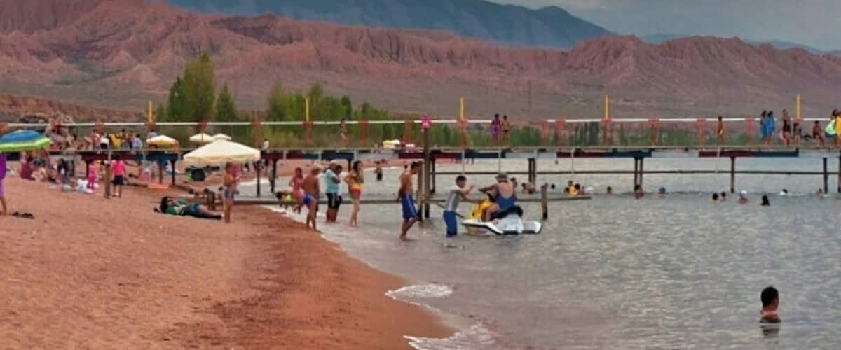 A beach with people, a body of water, and mountains in the background.