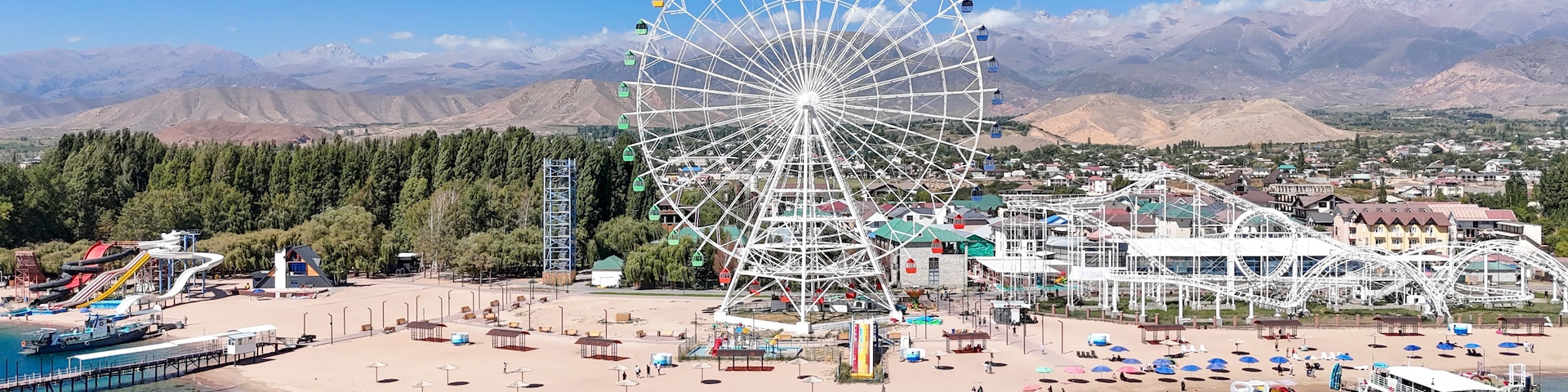 Un parque de atracciones costero con una noria gigante, parque acuático y una playa.