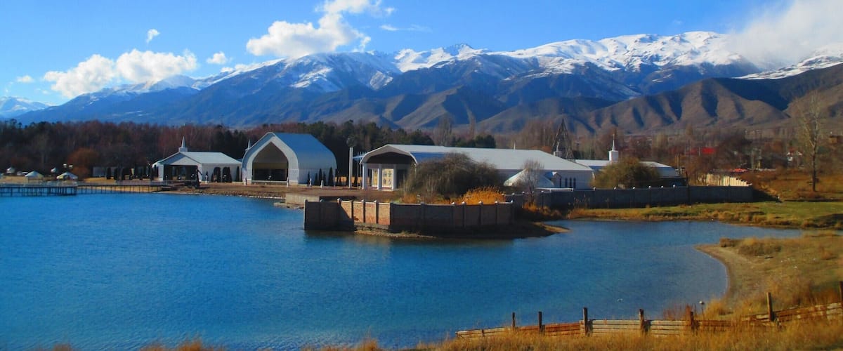 A lake with buildings and mountains in the background.