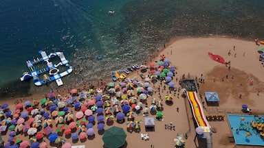 Une vue aérienne d’une plage bondée, avec des structures gonflables, des parasols colorés et un toboggan aquatique.