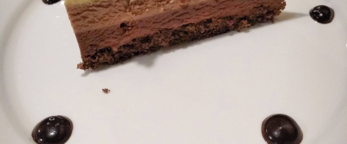 A slice of layered cake on a white plate with a mint leaf garnish.