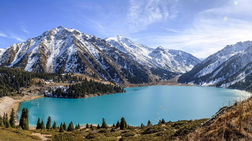 A turquoise lake surrounded by snow-capped mountains and dense forests.