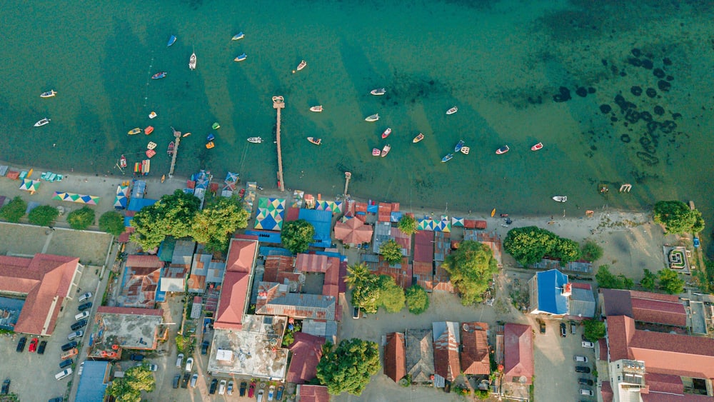 An aerial view of a coastal town with boats, colorful buildings, and a clear blue sea.