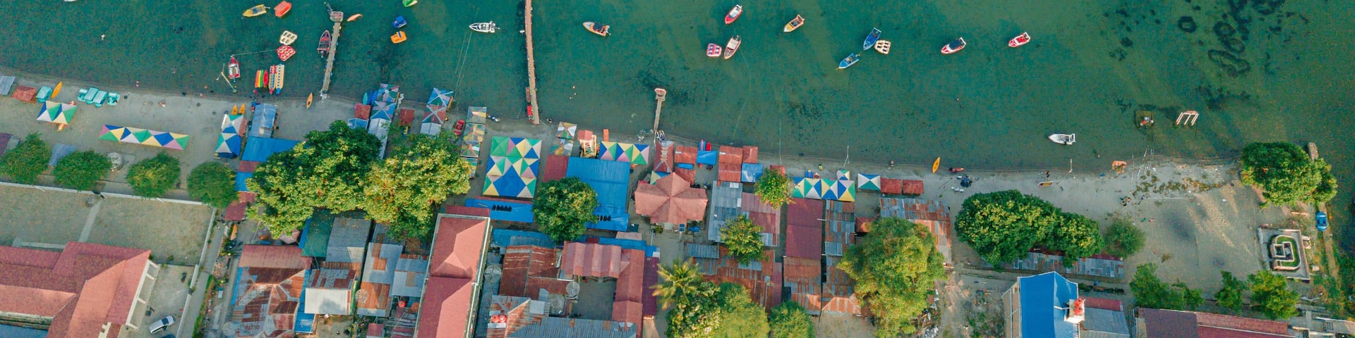 An aerial view of a coastal town with boats, colorful buildings, and a clear blue sea.
