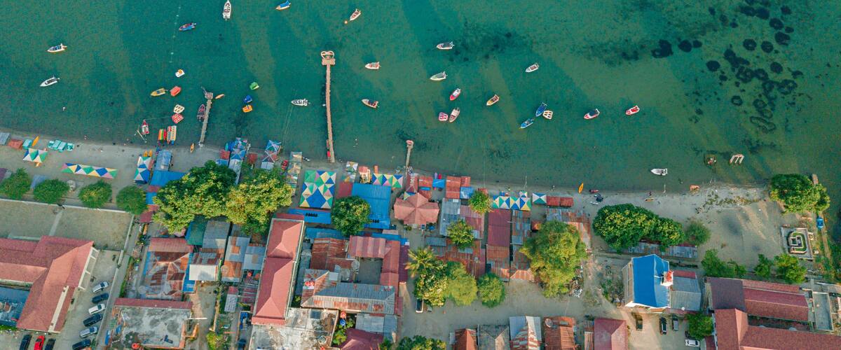 An aerial view of a coastal town with boats, colorful buildings, and a clear blue sea.