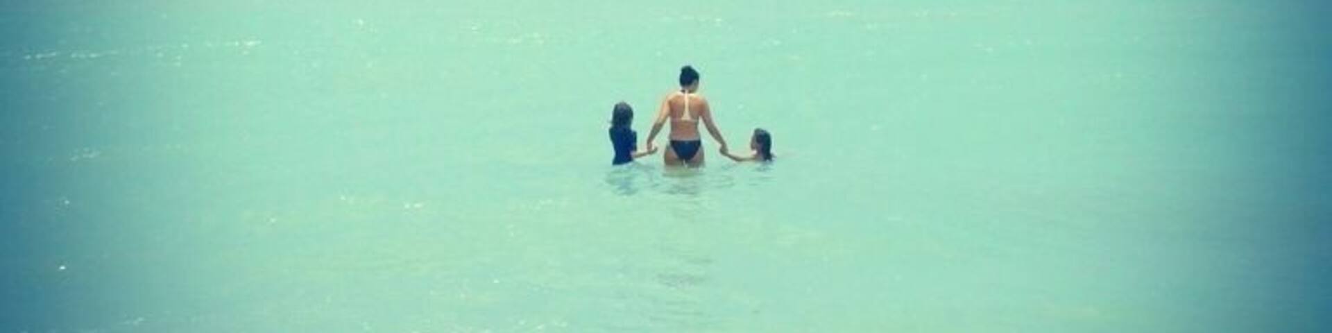 A person in the water with a child, surrounded by calm ocean waves.