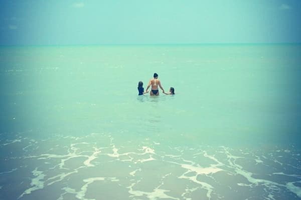 A person in the water with a child, surrounded by calm ocean waves.