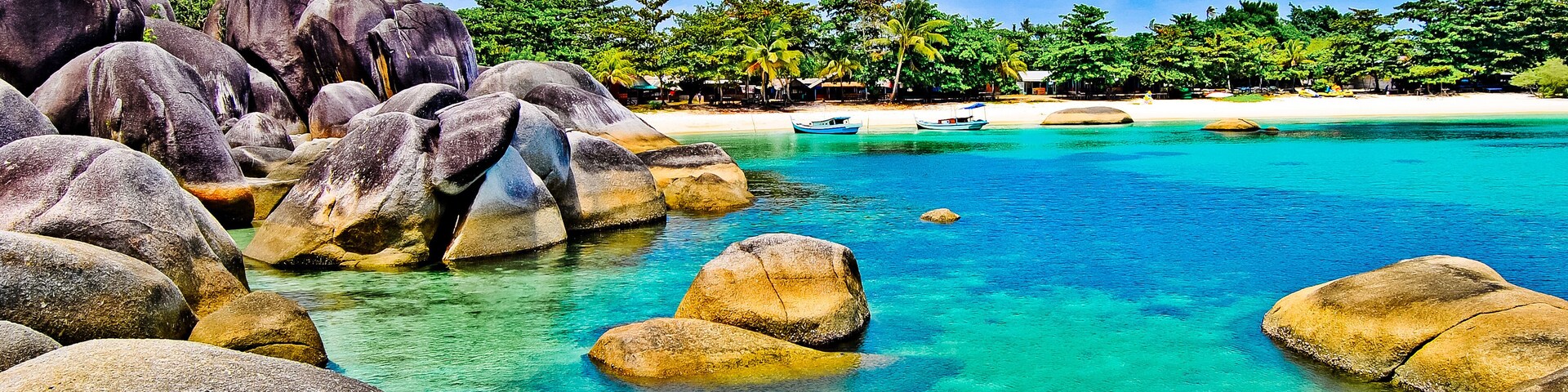 Una playa tropical con rocas grandes en el agua, agua turquesa cristalina y una playa de arena con palmeras.