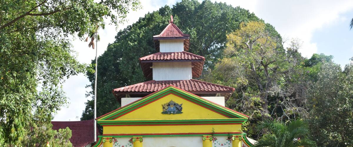 A temple with a red-tiled roof, yellow and green walls, and a central archway.