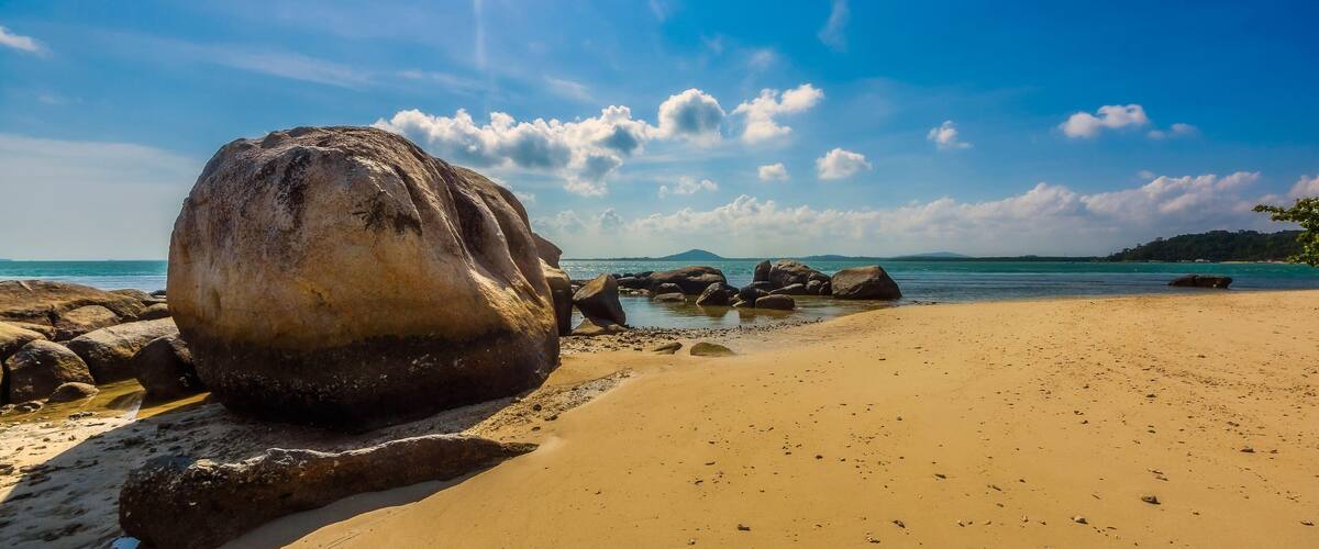 A large rock on a sandy beach with the ocean in the background.