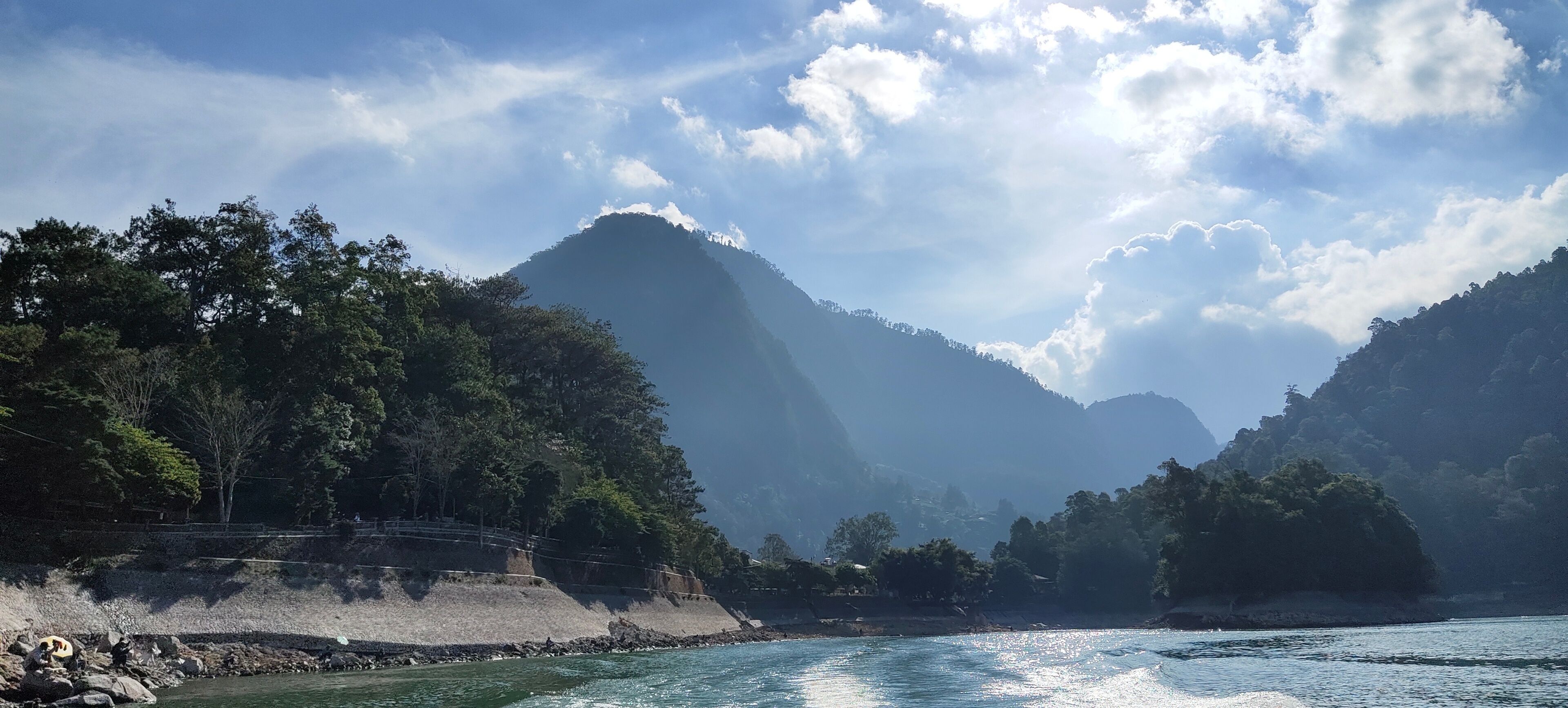 A river with a rocky shoreline, dense forest, and mountains in the background.
