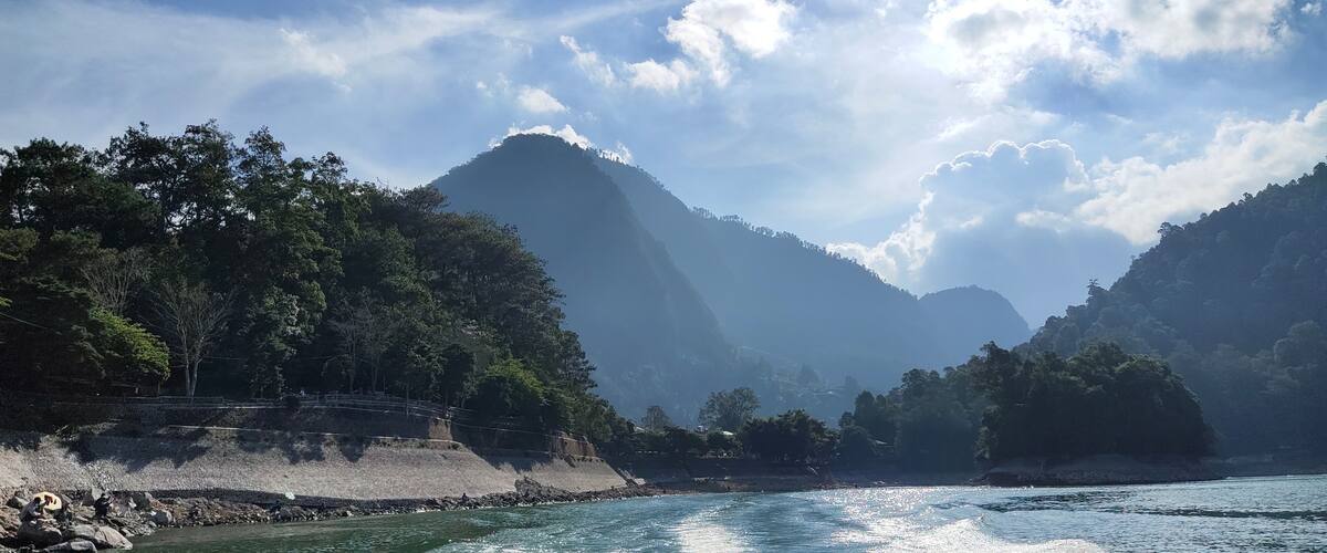 A river with a rocky shoreline, dense forest, and mountains in the background.
