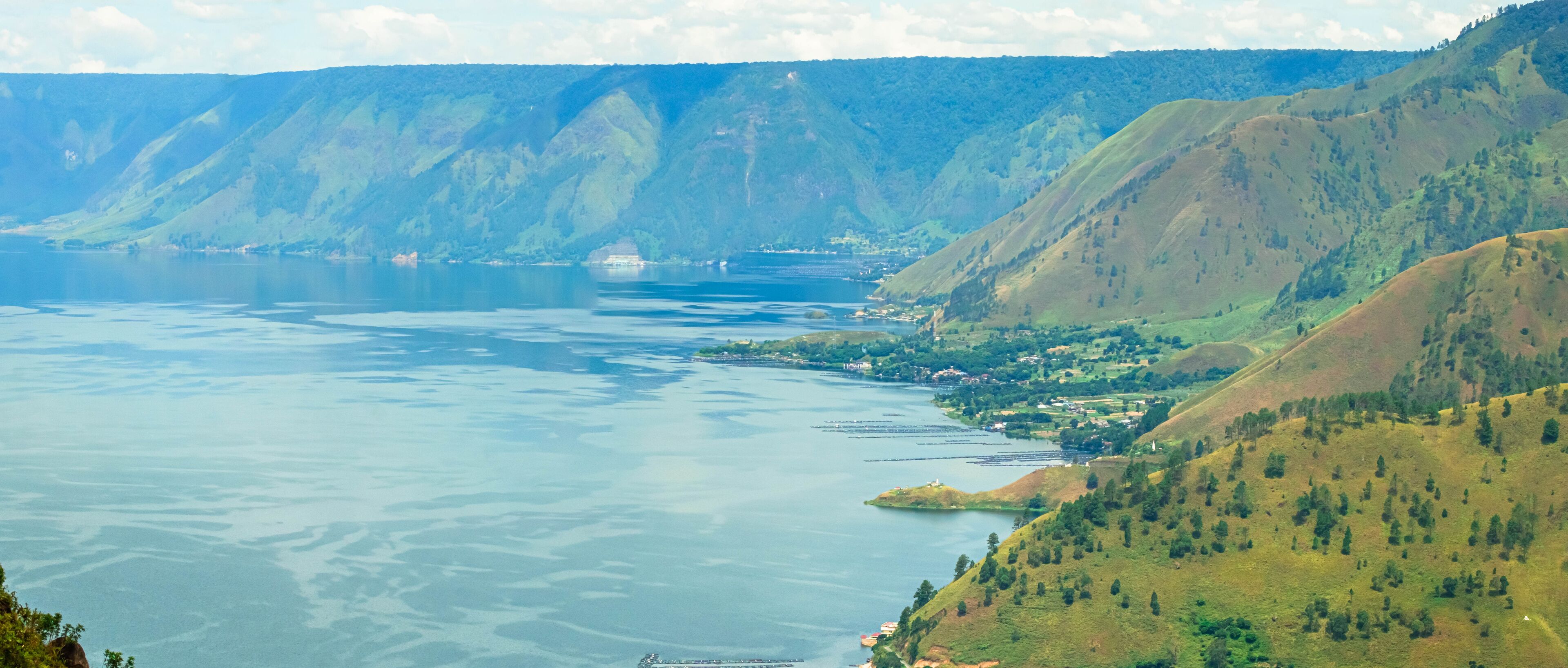 A panoramic view of a lake surrounded by green hills and mountains.