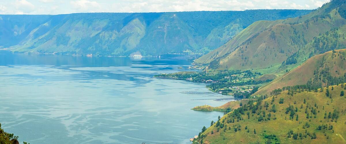 A panoramic view of a lake surrounded by green hills and mountains.