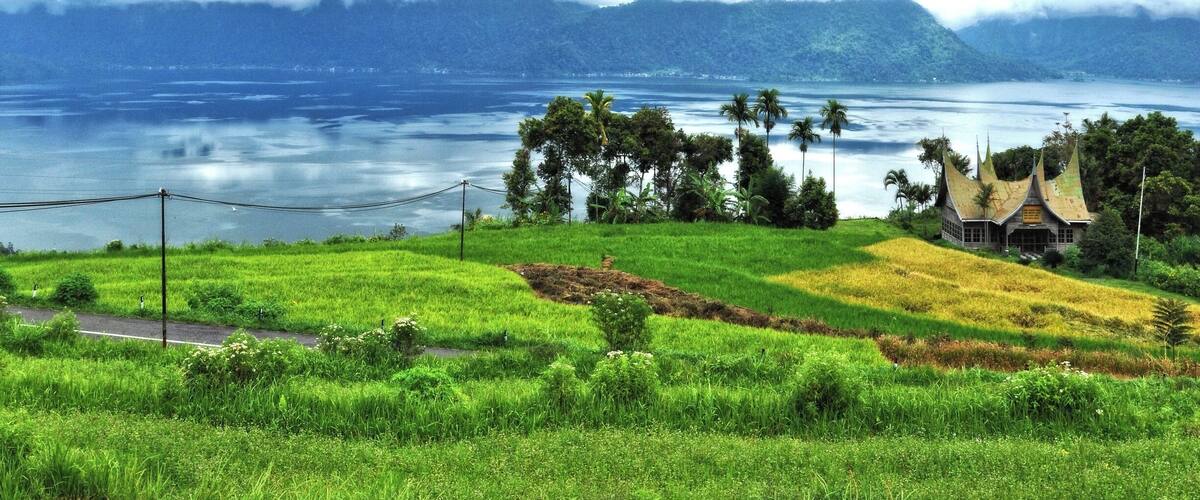 A coastal landscape with a house, green fields, and mountains in the background.