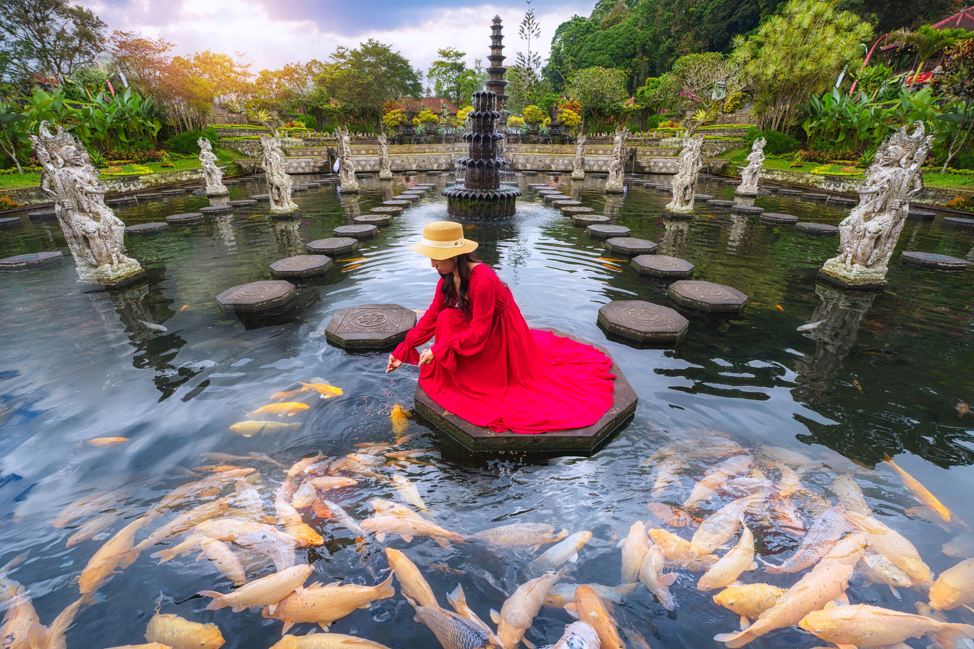 Female traveler feeds koi fish in Taman Tirtagangga Temple, Bali, Indonesia.