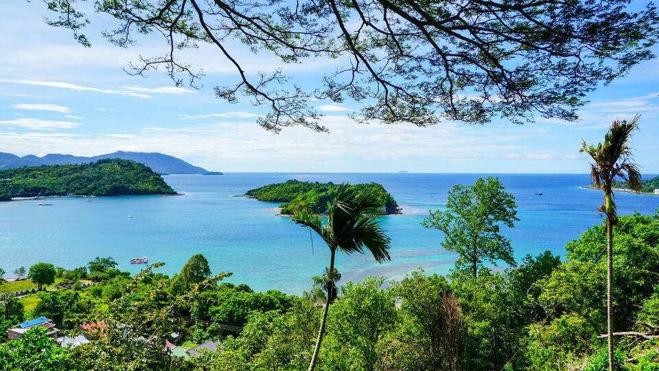 A coastal landscape with a clear blue sea, lush green islands, and a backdrop of mountains.