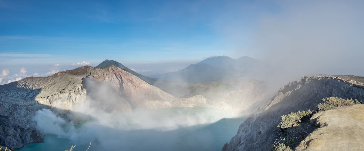 A volcanic crater with a lake surrounded by rugged mountains and mist.