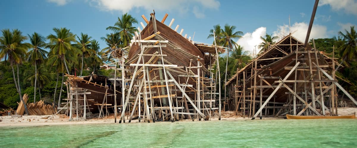 A beach with wooden structures under construction, palm trees, and clear turquoise water.