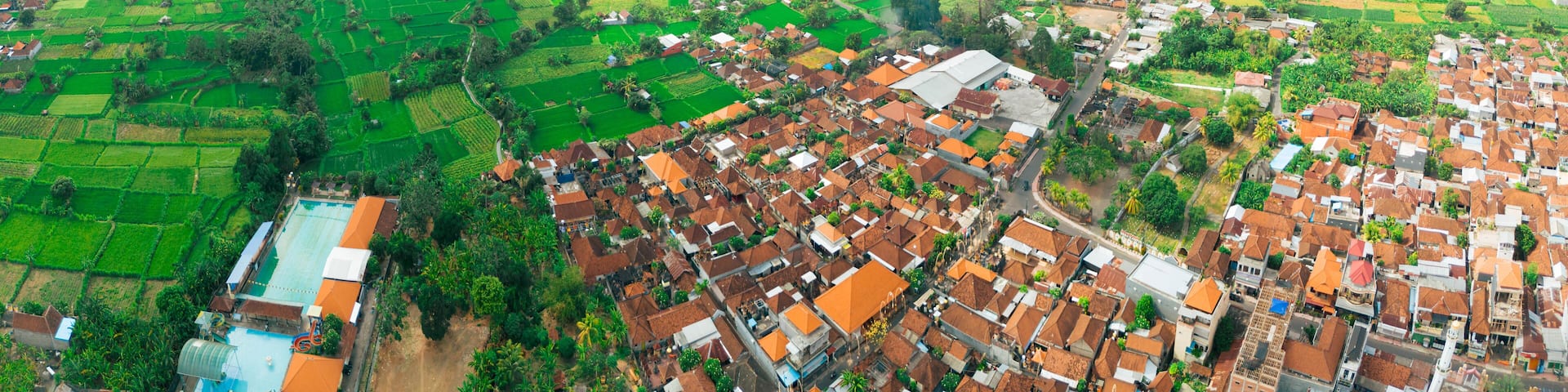 Panoramic aerial drone view of Muslim Balinese settlements near green paddy fields scenery at Gelgel Village in Klungkung, Bali, Indonesia.