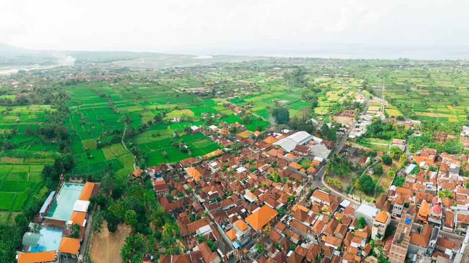 Panoramic aerial drone view of Muslim Balinese settlements near green paddy fields scenery at Gelgel Village in Klungkung, Bali, Indonesia.