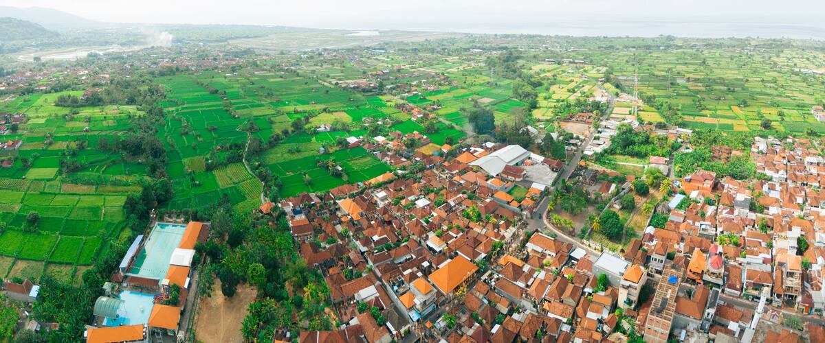 An aerial view of a rural landscape with green fields, a river, and a cluster of houses with red roofs.