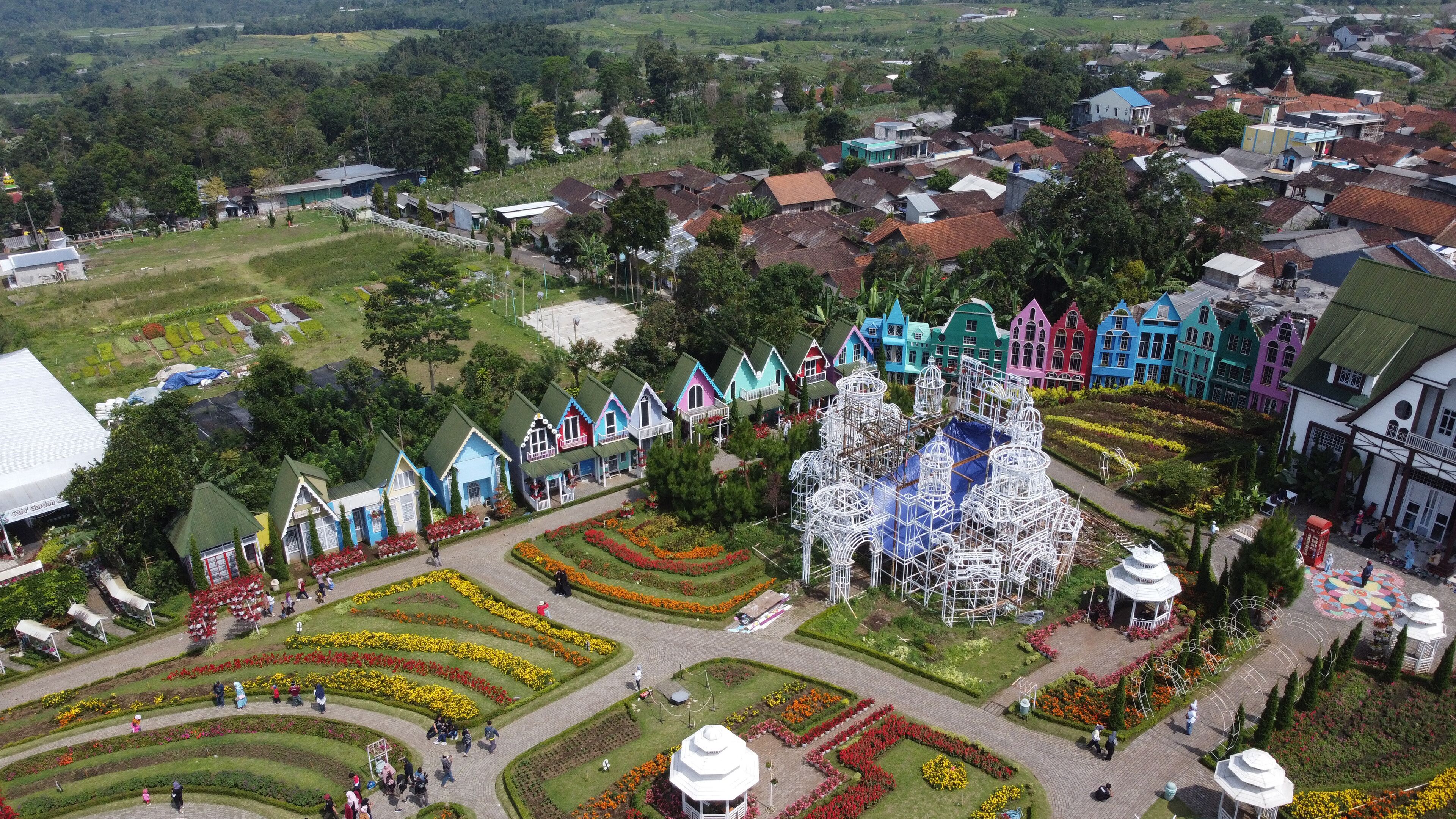 A colorful village with unique architecture, a large white structure, and well-maintained gardens.