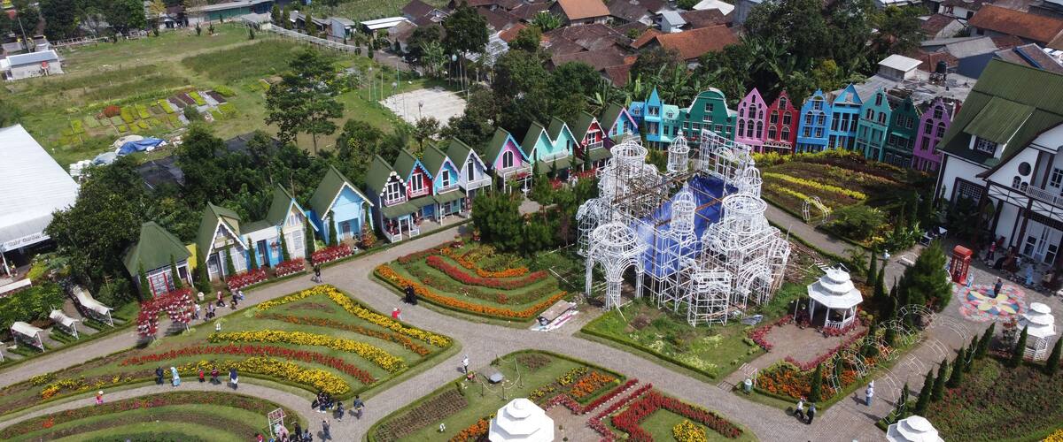A colorful village with unique architecture, a large white structure, and well-maintained gardens.