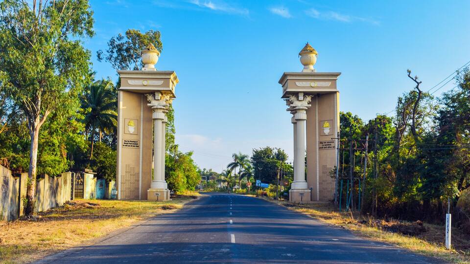 A road flanked by two large columns with inscriptions, leading to a gate.