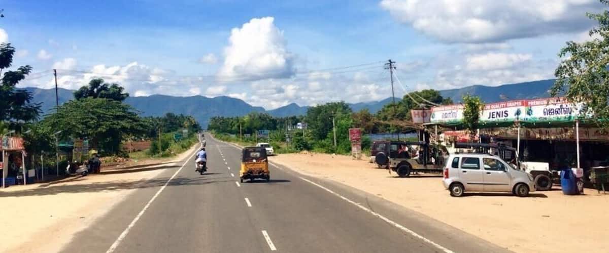 A road with vehicles, roadside shops, and mountains in the background.