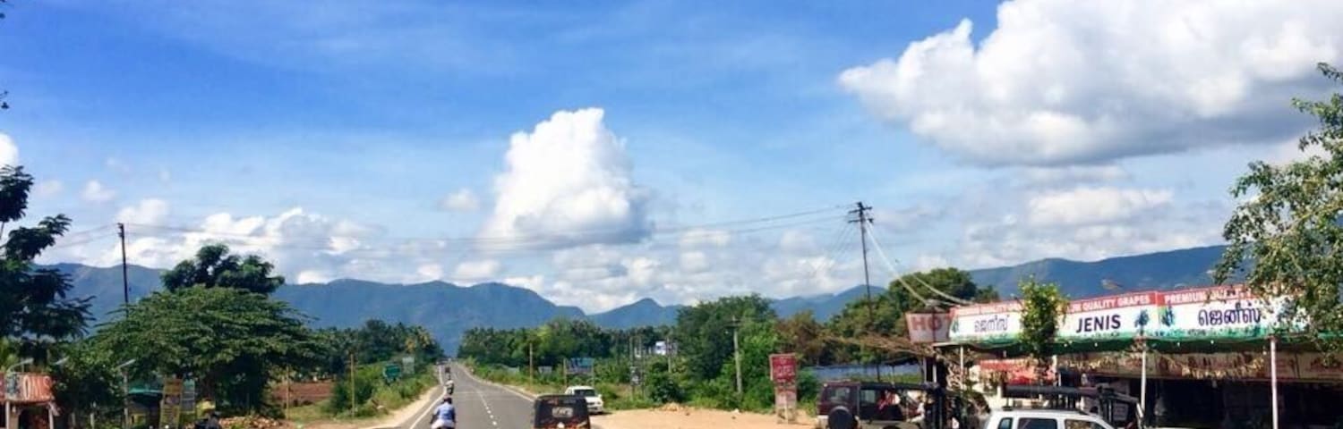 A road with vehicles, roadside shops, and mountains in the background.