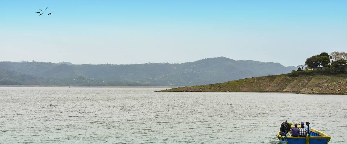 A calm lake with a small boat carrying people, surrounded by hills and a clear sky.