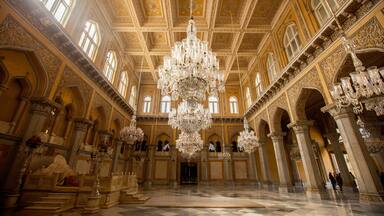 An ornate hall with a large chandelier, intricate ceiling designs, and classical architecture.