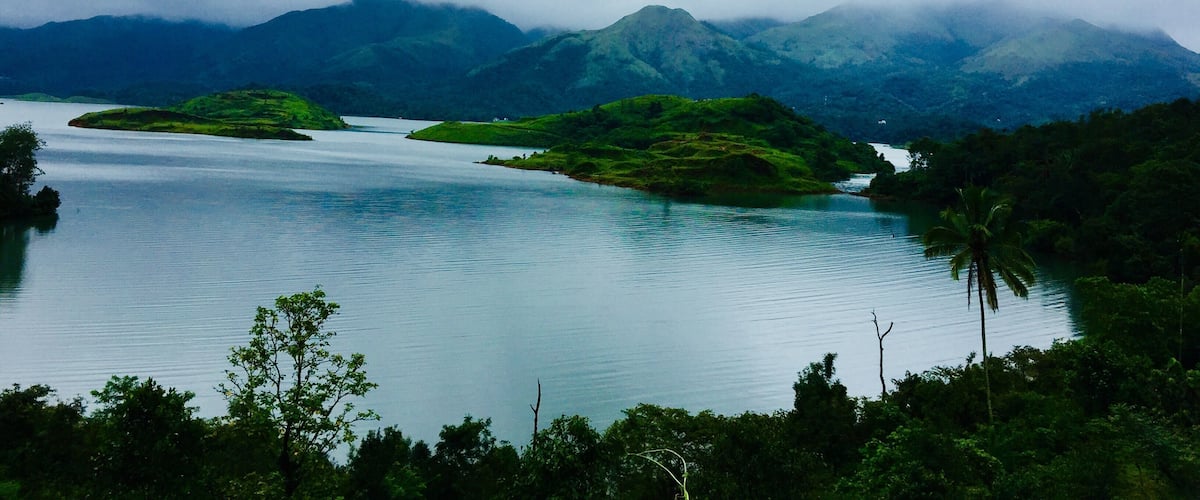 A calm lake surrounded by lush green hills and mountains under a cloudy sky.