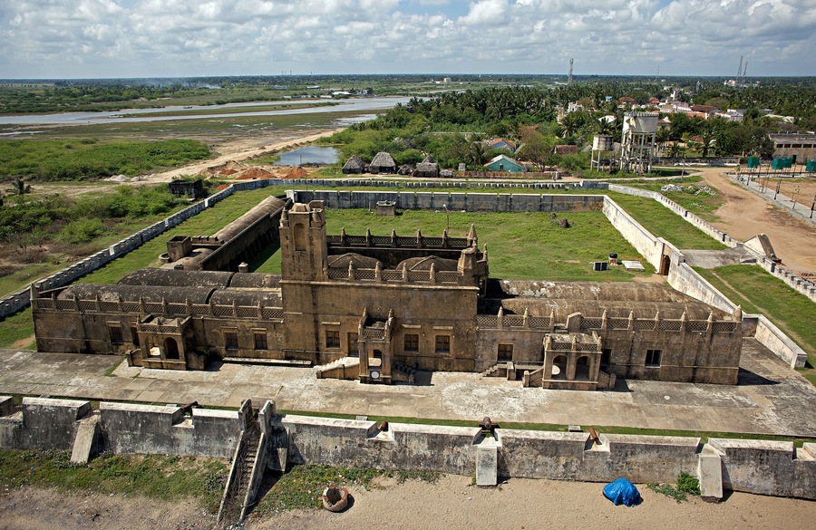 Aerial view of a historical fort stands with weathered stone against a backdrop of wetlands and distant buildings, Tharangambadi, Tamil Nadu, India.