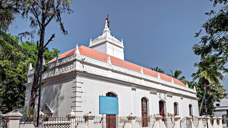 A white colonial-style building with a red roof, arched windows, and a decorative tower.
