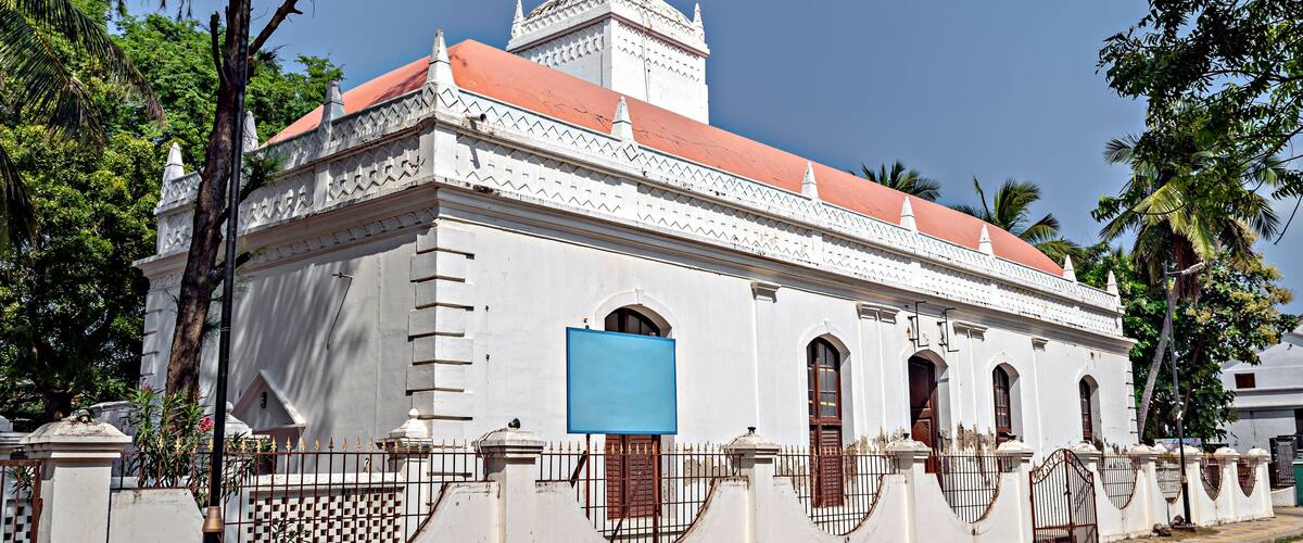 A white colonial-style building with a red roof, arched windows, and a decorative tower.