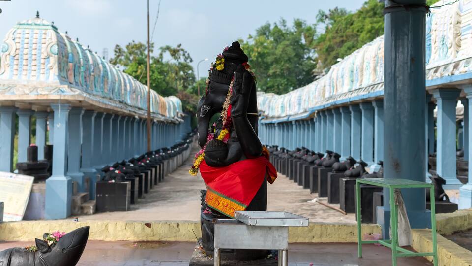 A statue of a deity in a temple corridor with blue pillars and a tiled floor.