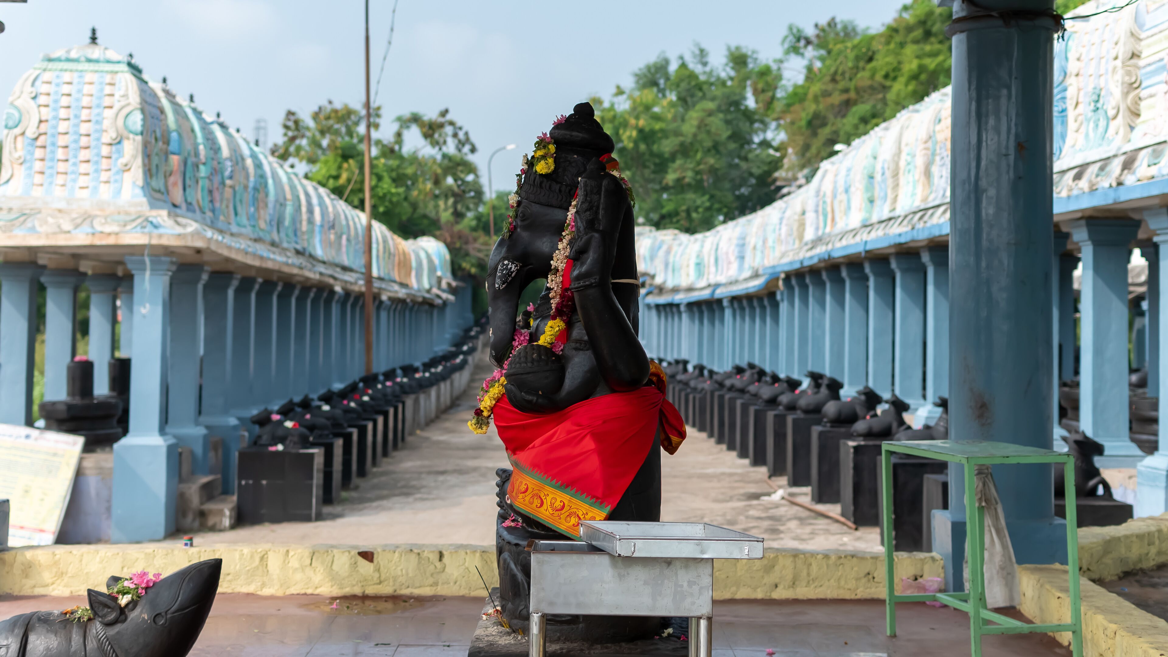 A statue of a deity in a temple corridor with blue pillars and a tiled floor.