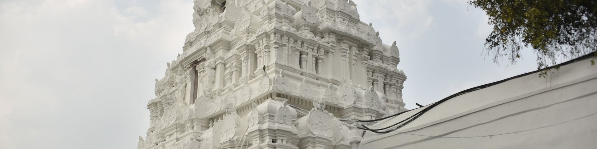 A white temple with intricate carvings and a golden statue in front.