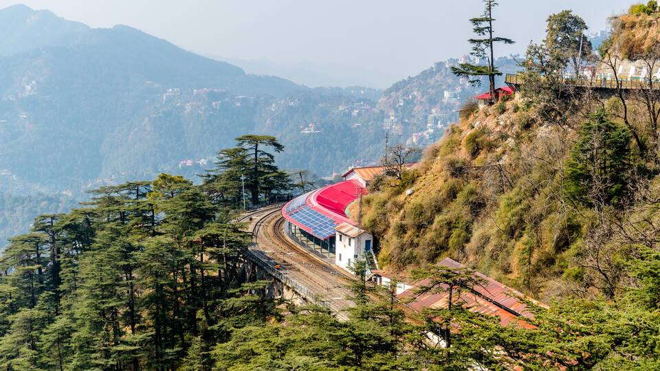 A railway track curving through a mountainous landscape with a red-roofed building on a hillside.