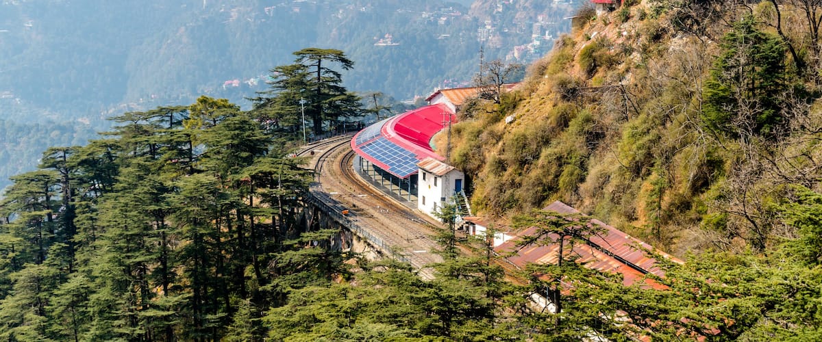 A railway track curving through a mountainous landscape with a red-roofed building on a hillside.