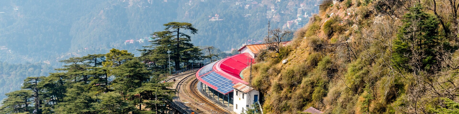 A railway track curving through a mountainous landscape with a red-roofed building on a hillside.