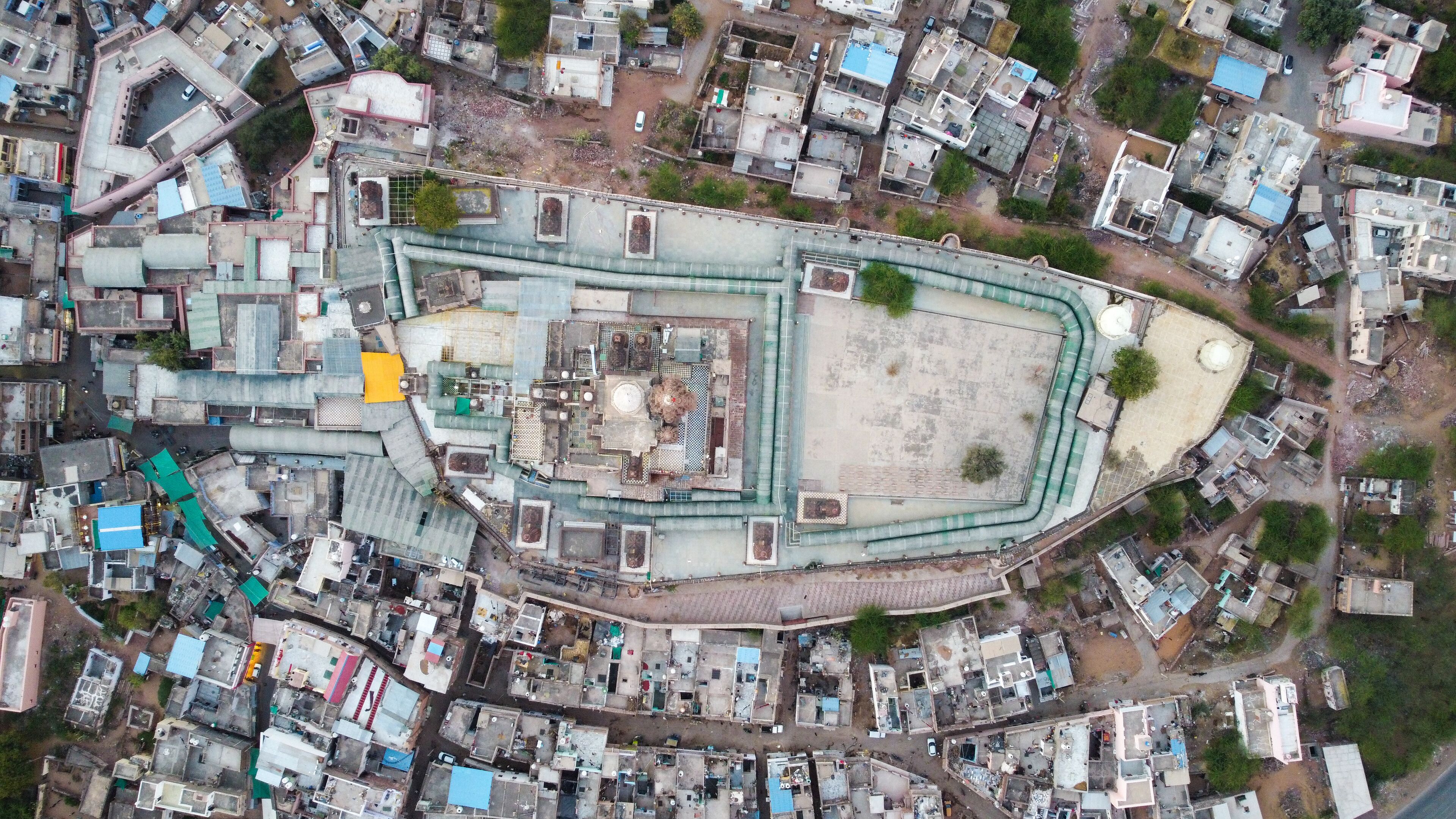 An aerial view of a densely packed urban area with a large, irregularly shaped building surrounded by smaller structures.