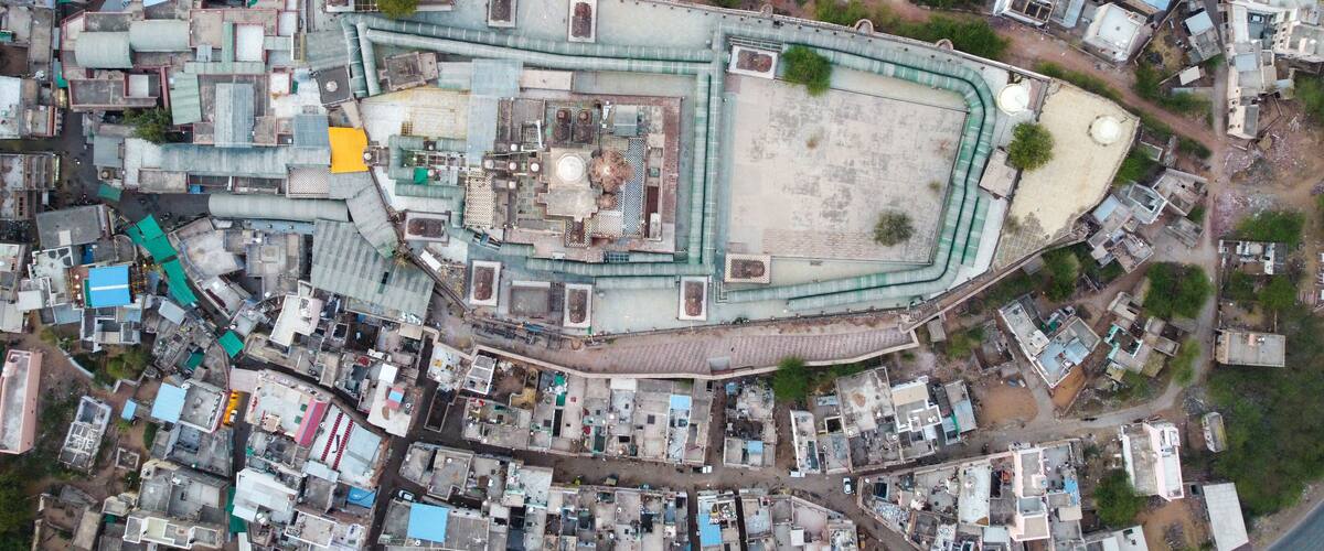 An aerial view of a densely packed urban area with a large, irregularly shaped building surrounded by smaller structures.