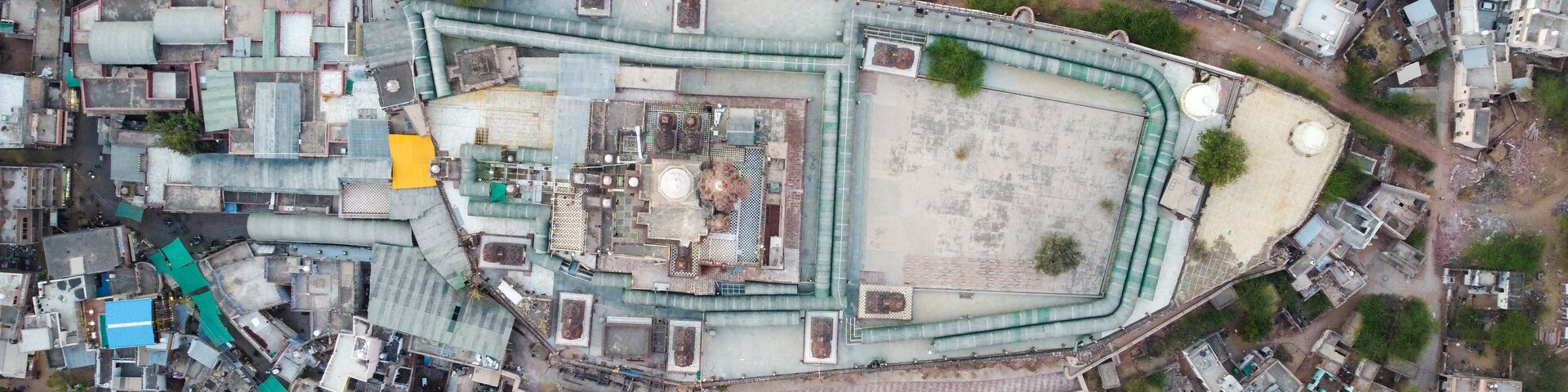 An aerial view of a densely packed urban area with a large, irregularly shaped building surrounded by smaller structures.